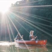 Students canoeing on a river with the sun shining over the trees