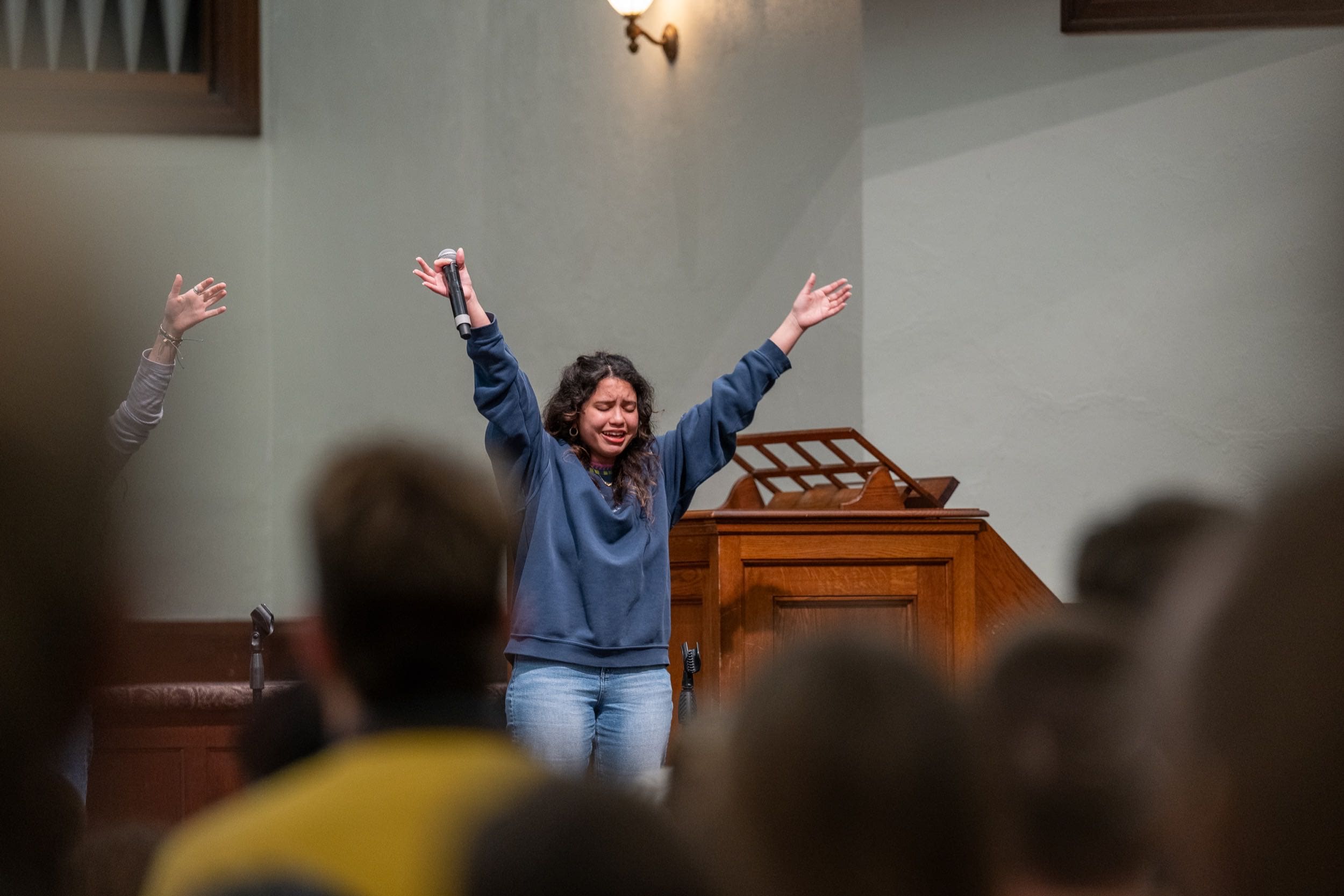 A female Asbury student worships in chapel with arms extended
