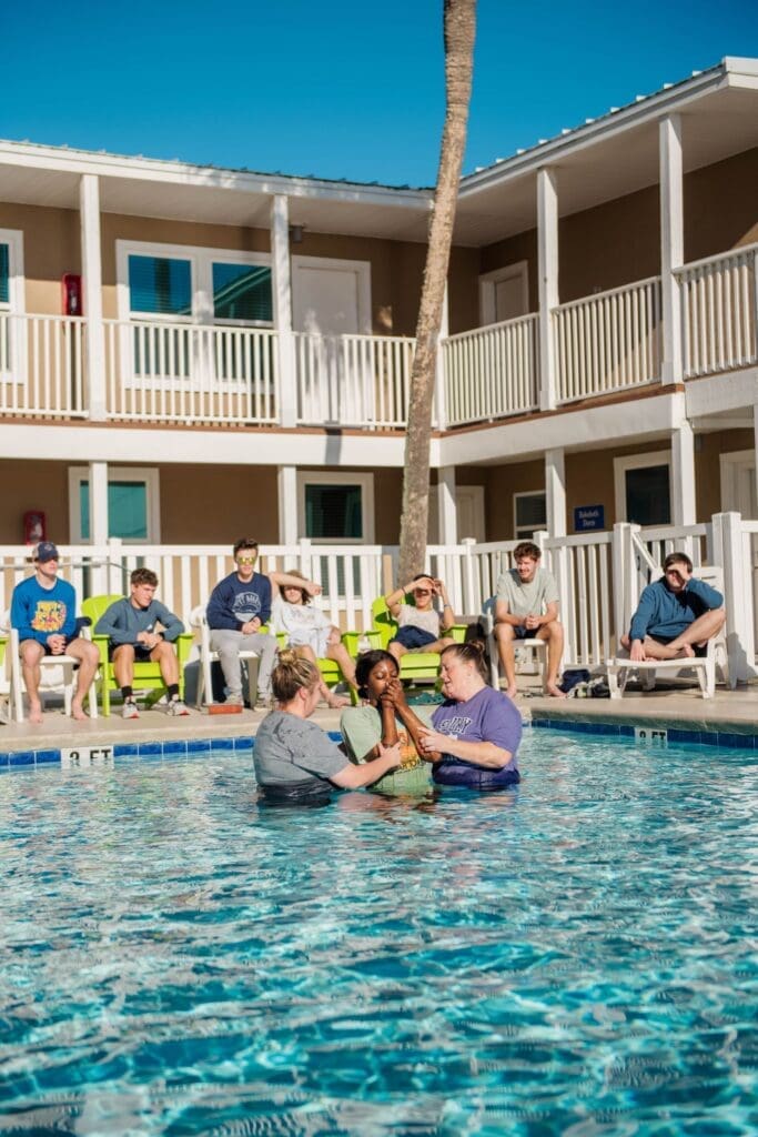 Two Asbury members baptize a female student in an outdoor pool at a Set Apart retreat as others look on