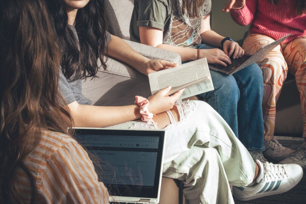Close up of books and laptops resting on laps as students study.