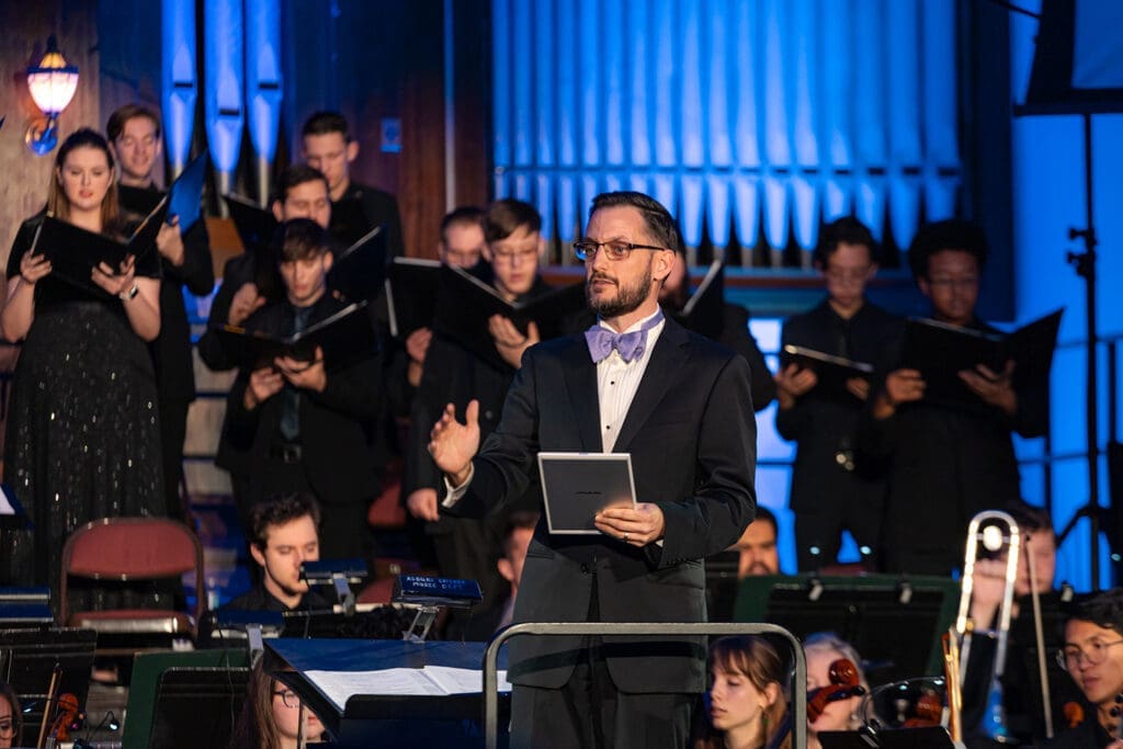 Male Asbury music professor with bowtie conducts a student choir and orchestra