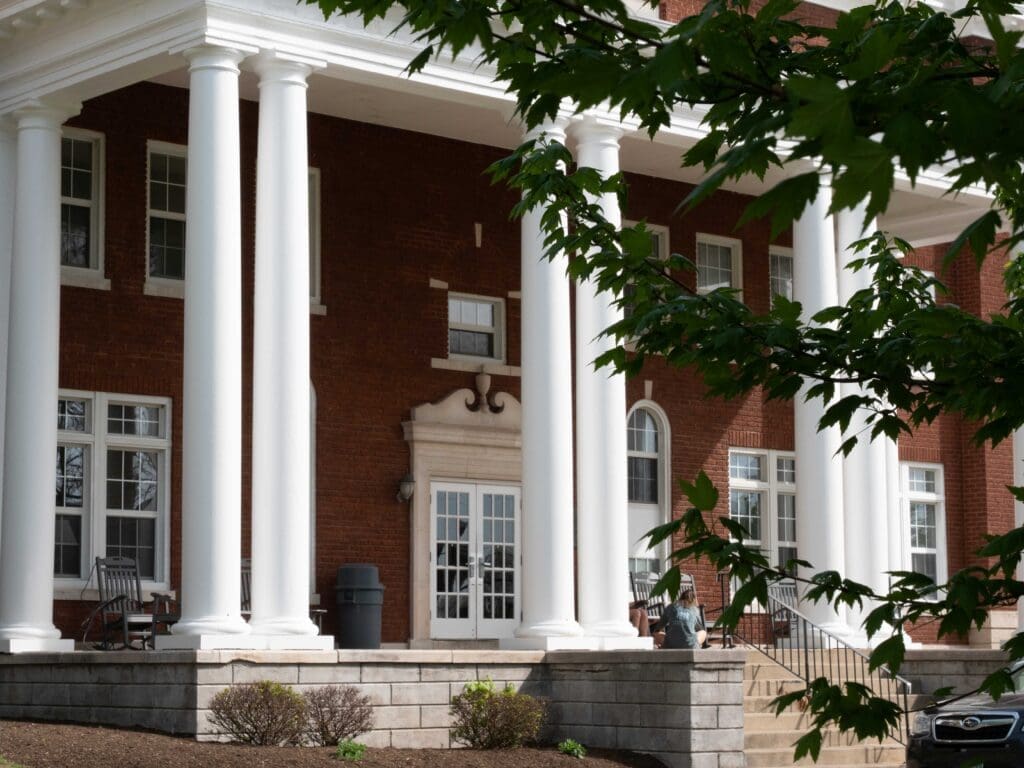 Front entrance of Glide-Crawford Hall at Asbury University, partially obscured by trees, a historic residence hall built in 1924.