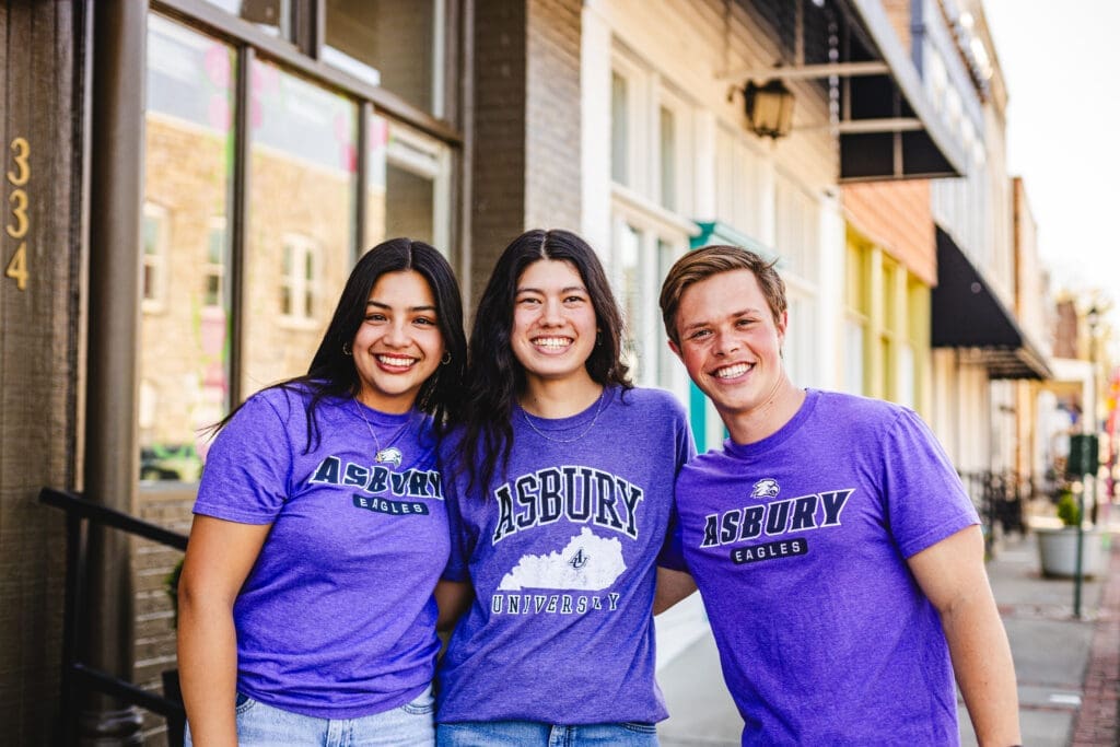 Three students wearing Asbury purple shirts on the campus of Asbury University.