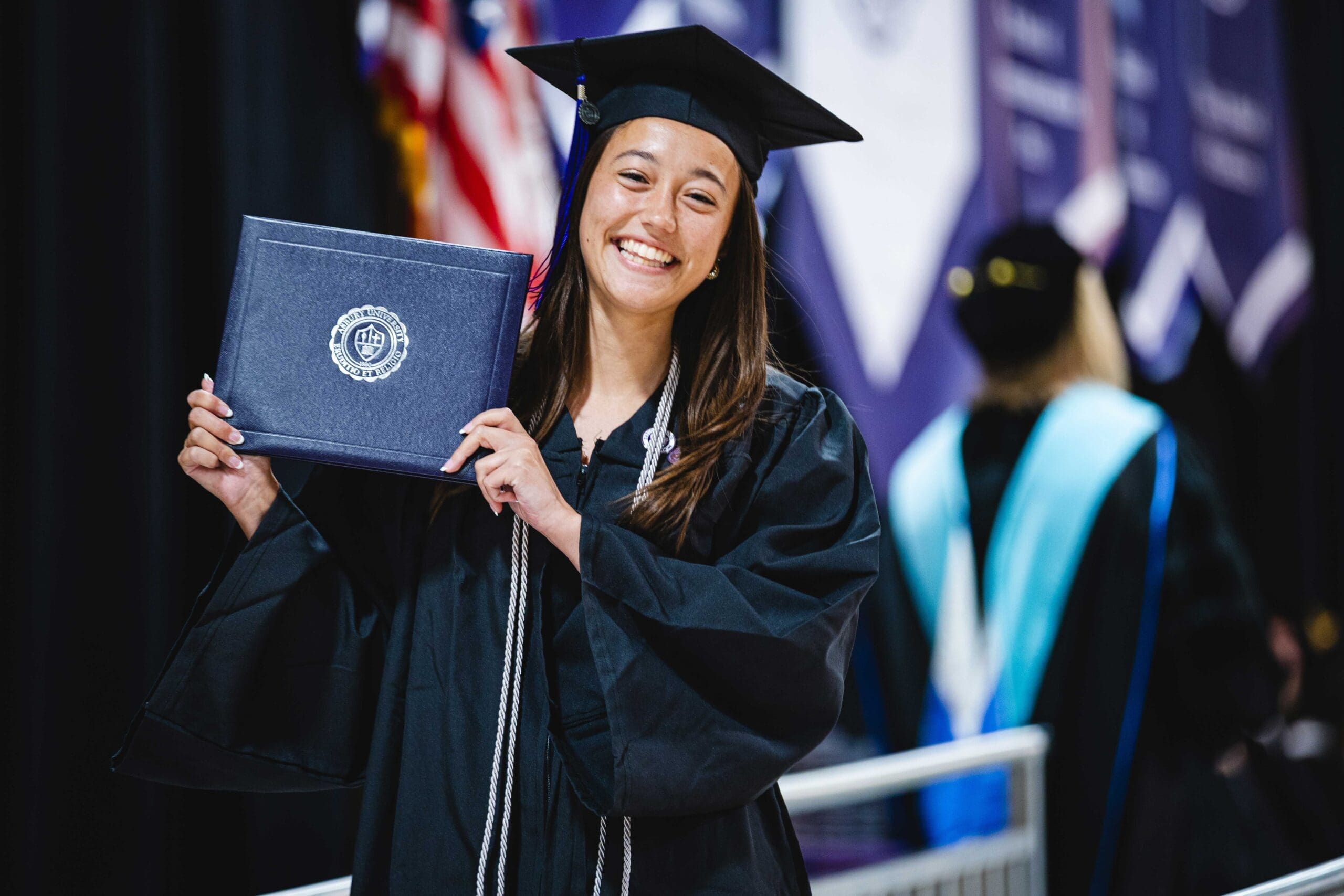 Asbury graduate smiling and holidng up diploma at graduation.