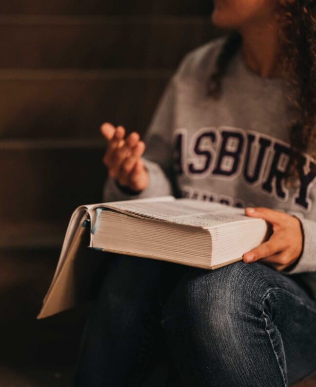 Asbury student with Bible open sitting and communicating with her hands.