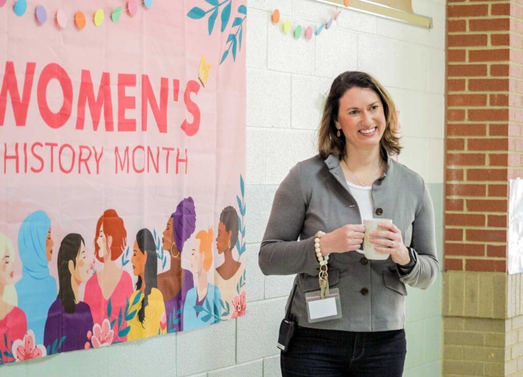 Asbury graduate educator standing in a school with a Women's History Month sign behind her.