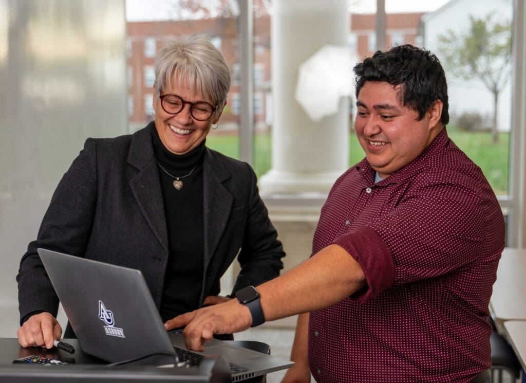 Two educators standing side by side on Asbury's campus looking at a computer monitor.