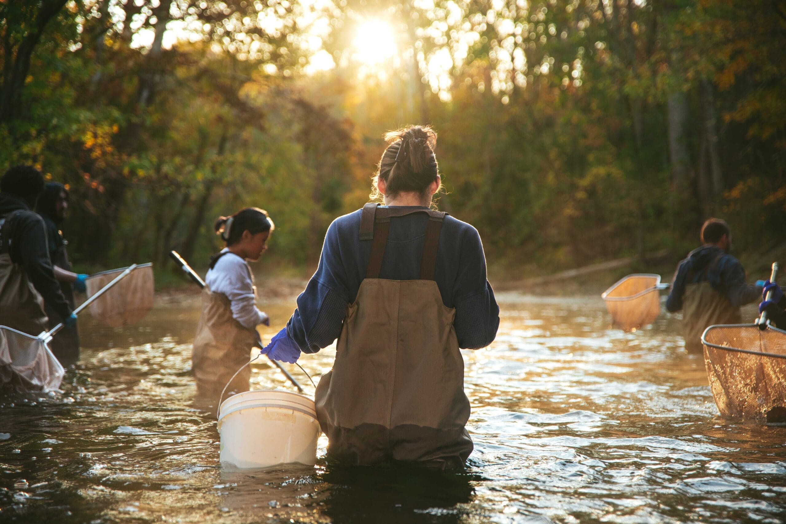 Female Asbury Biology student on a field trip in a creek. Sun shining on the water.
