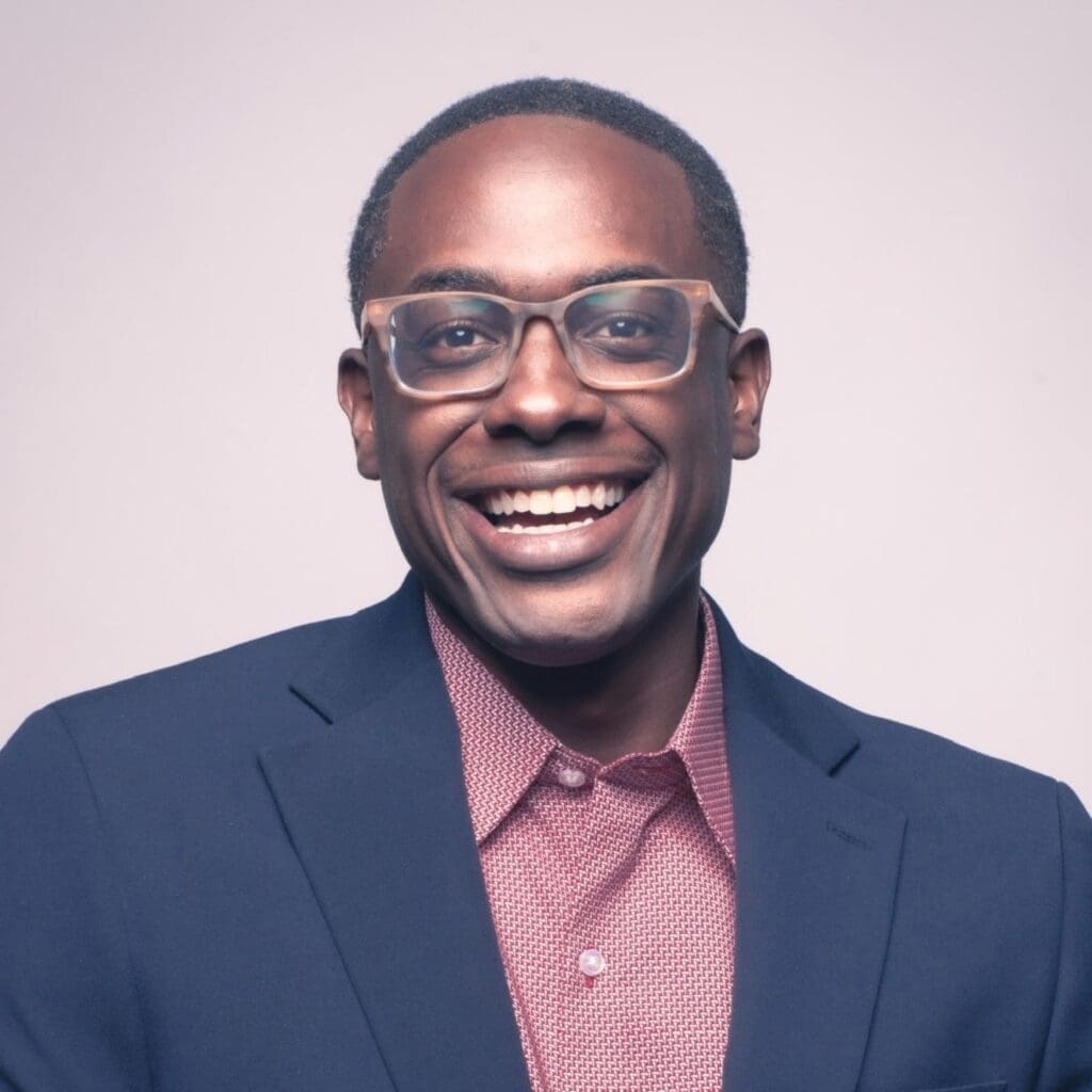 headshot of Shawn Okpebholo, smiling in a suit jacket wearing glasses