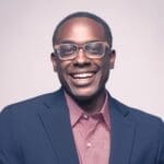 headshot of Shawn Okpebholo, smiling in a suit jacket wearing glasses