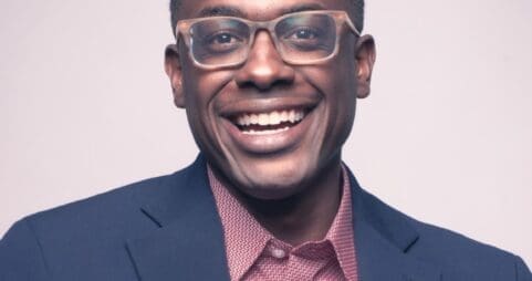 headshot of Shawn Okpebholo, smiling in a suit jacket wearing glasses