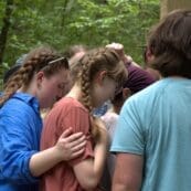 High school students praying in a group in a forest