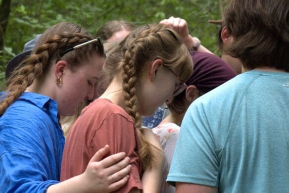 High school students praying in a group in a forest