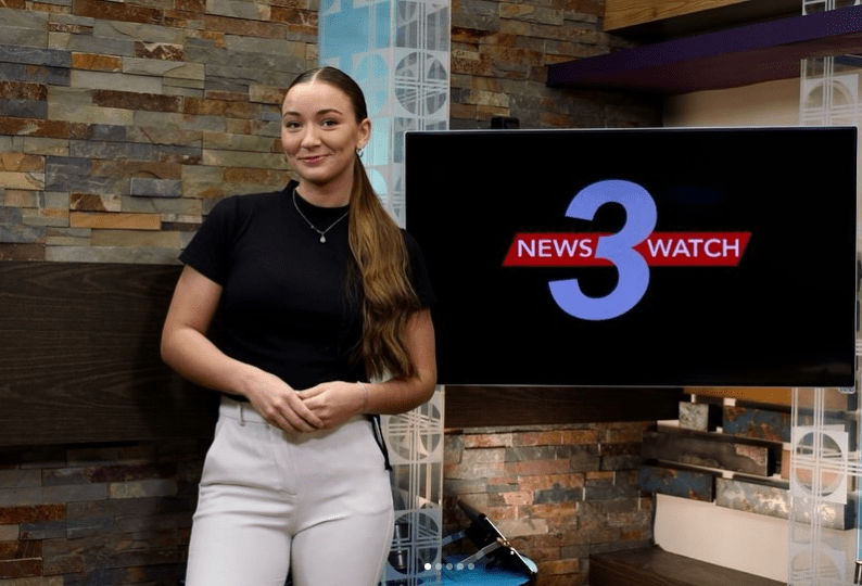 Female Asbury student anchors the newswatch production next to tv