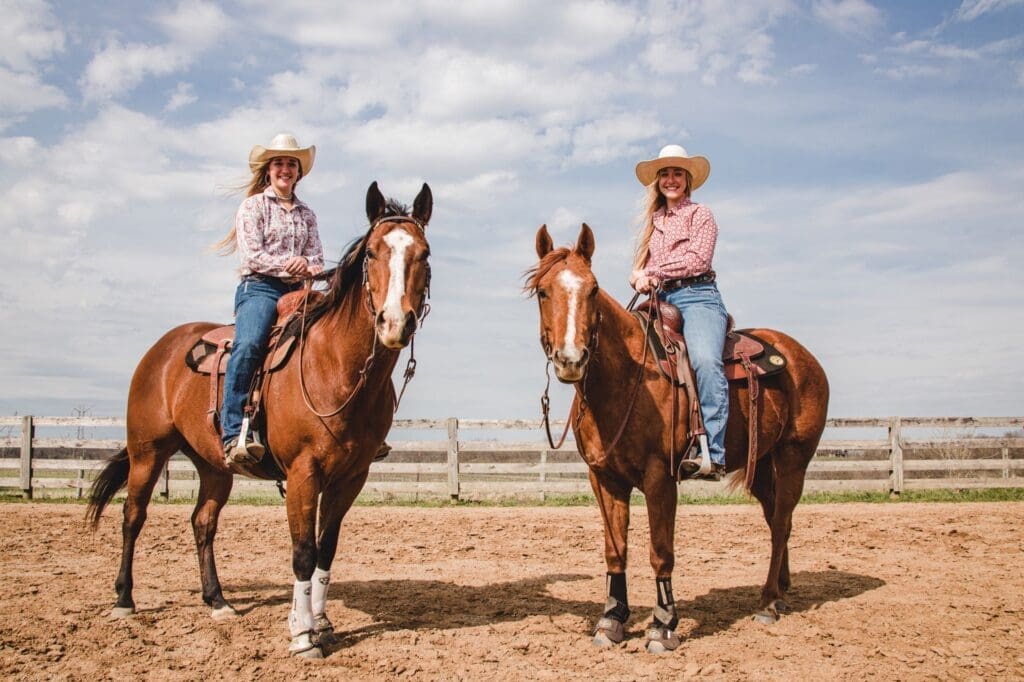 Two female students with matching cowboy hats on horses at the Equine farm.