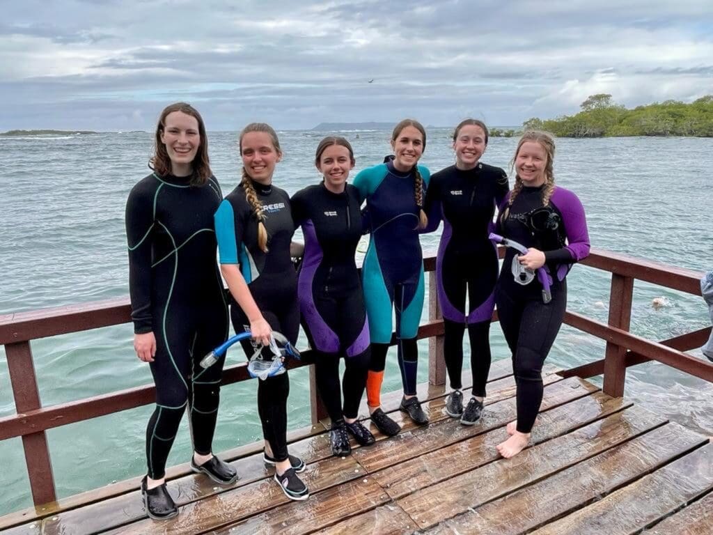 Small group of Asbury students stand in wetsuits on a dock in a tropical ocean setting