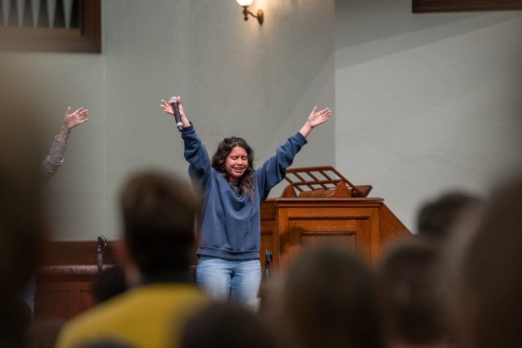 A female Asbury student worships in chapel with arms extended