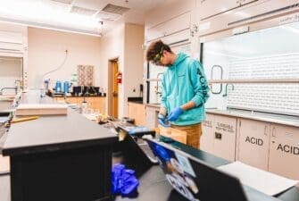 Male student in teal shirt uses equipment in chemistry lab