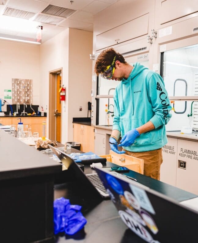 Male student in teal shirt uses equipment in chemistry lab