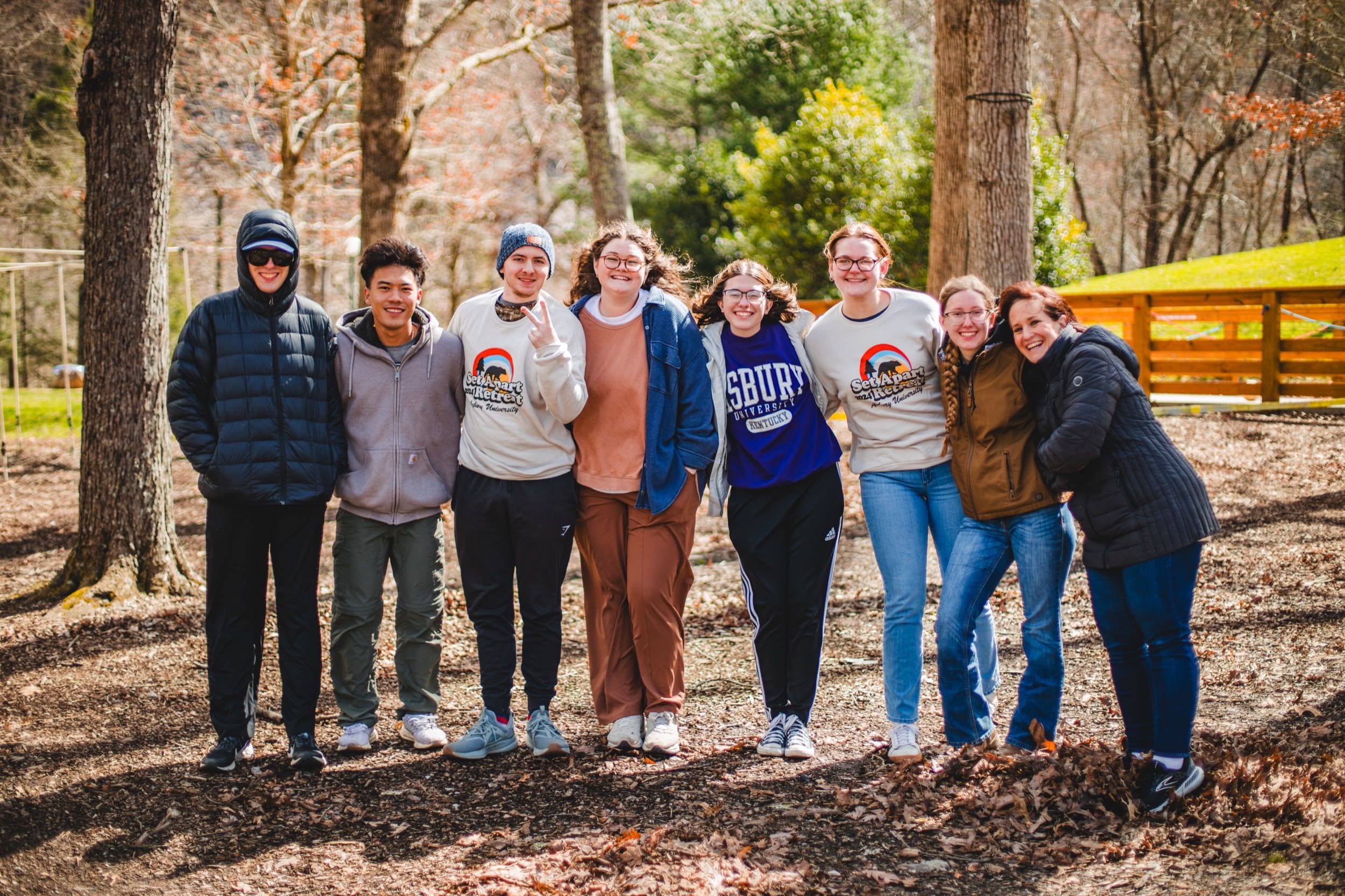 A small group of male and female Asbury students poses in an outdoor forest setting