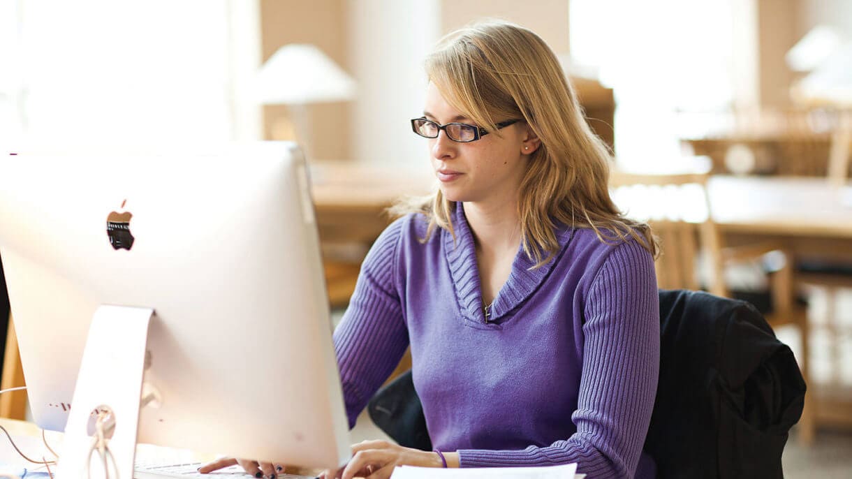 Woman in purple sweater uses computer at a desk