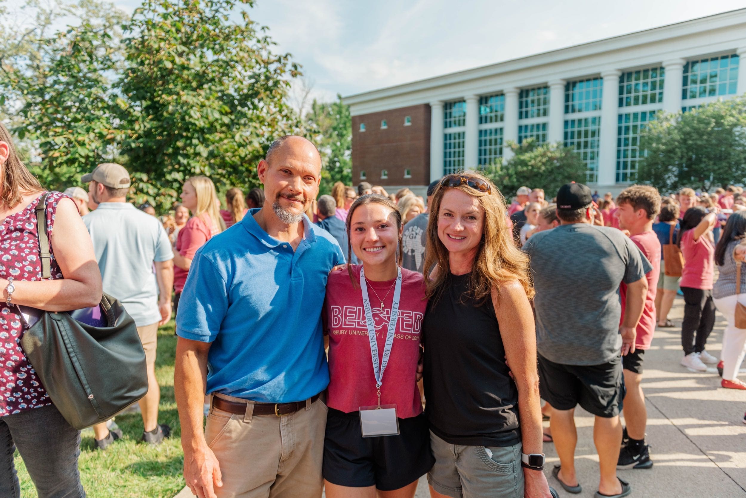 A dad in a blue shirt, mom in a black shirt stand on either side of their daughter outside at AU orientation