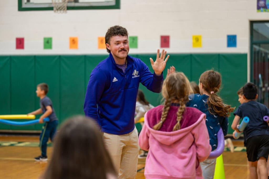 Asbury education student high-fiving kids as they walk by in the Luce Center