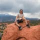 Male Asbury student sits on a red rock with the Colorado mountains in the background