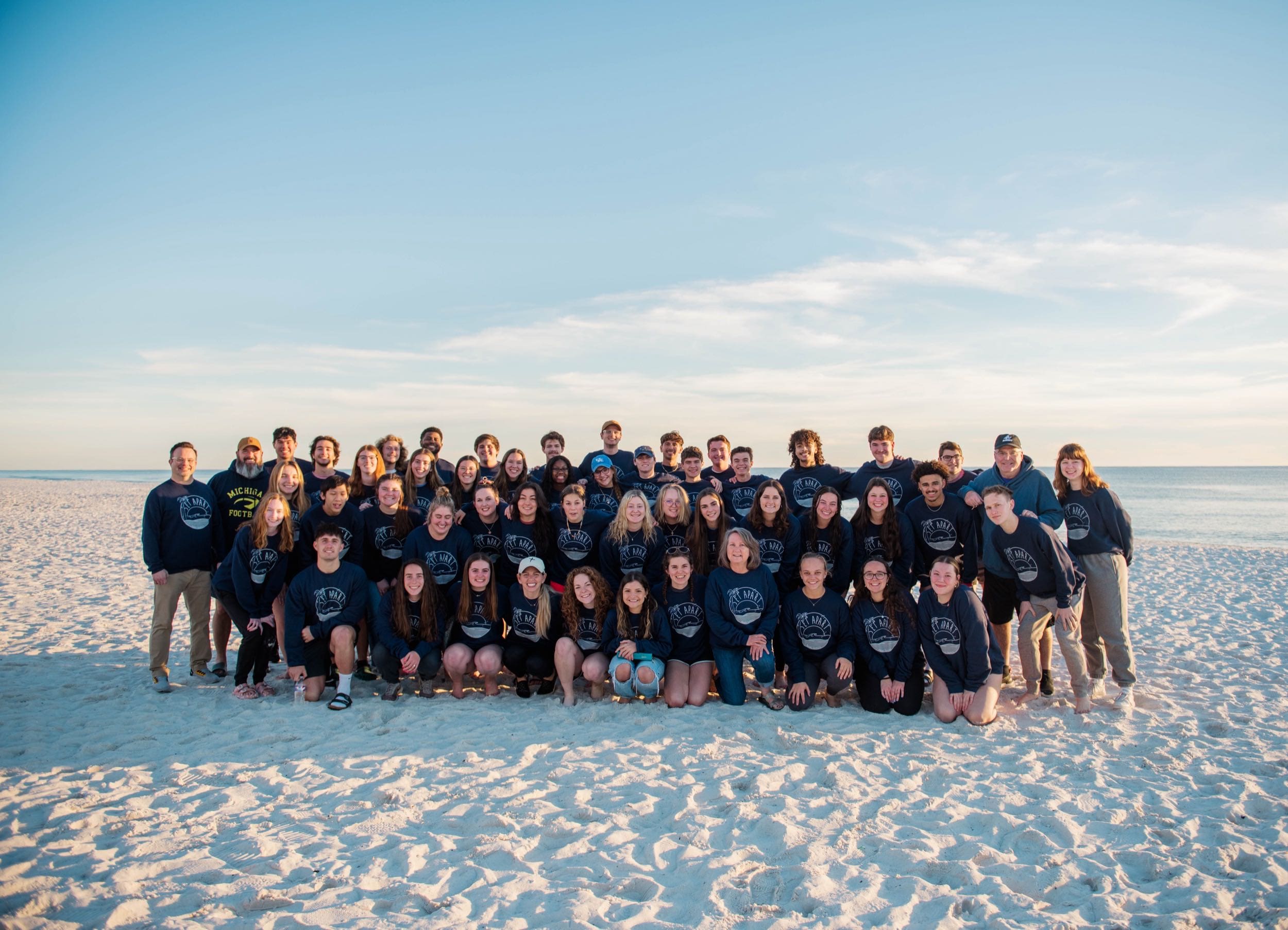 Large group of several dozen Asbury students poses together on the beach