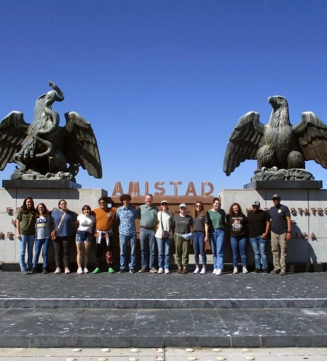 Students pose outside a monument of two alrge eagles