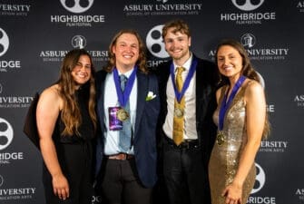 Four students with medals pose in front of a Highbridge film festival backdrop at the red carpet