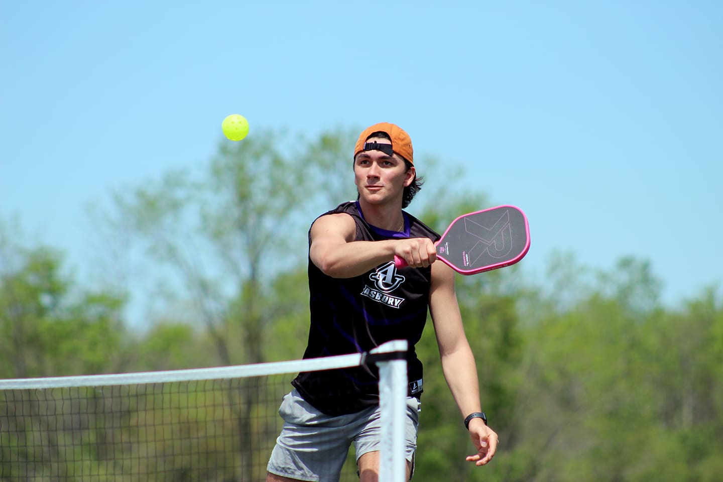 Asbury tennis player serves the ball on an outdoor court with blue sky