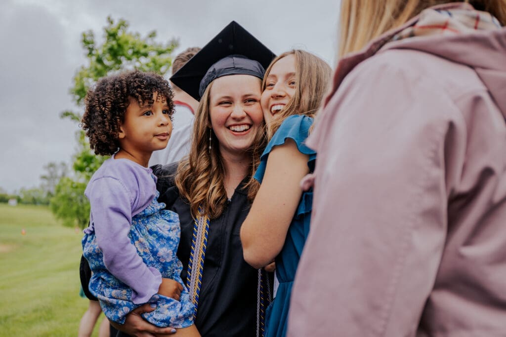 Asbury graduate holding her child and hugging someone.